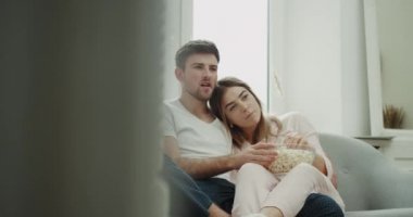 Romantik zaman çift kanepede oturan ve patlamış mısır ve mutlu harcama sabah birlikte yemek tv izlerken pijamayla sarılma.