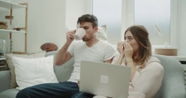 Kanepede oturan ve hasta gribi ve kötü, adam onu tutan onun kadın destekleyen öksürük var sabah birkaç içinde pijama, o ona e-posta kontrol ediyor defter--dan o sıcak bir içecek içmek.