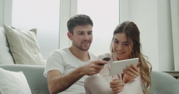 Retrato de pareja joven carismática que pide algo de la tableta usando un teléfono para confirmar el orden diseño moderno . — Vídeos de Stock