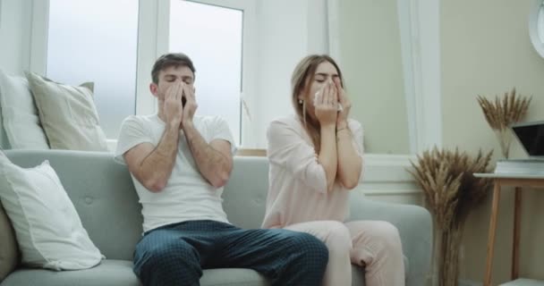 En el sofá una bonita pareja joven en pijama tiene una gripe sintiéndose mal usando pañuelos para la secreción nasal . — Vídeo de stock