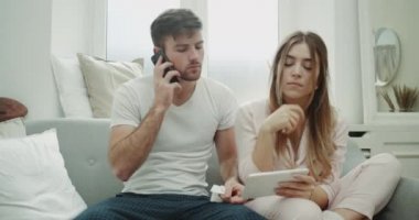 Genç bir çift pijama için grip zaman oturup kanepe öksürük ve kötü hissediyor bir tablet ve cep telefonu kullanarak bir şey sipariş.