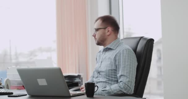 Щасливий офіс менеджер посміхається перед камерою і показує великий, як сидіти на його офісному стільці. 4k — стокове відео