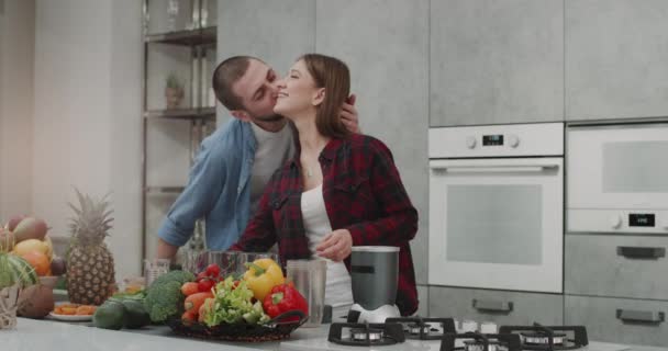 No casal da manhã preparando juntos o smoothie para um café da manhã saudável em um design de cozinha moderna, toda a mesa da cozinha está decorada com legumes e frutas para o café da manhã saudável. . — Vídeo de Stock