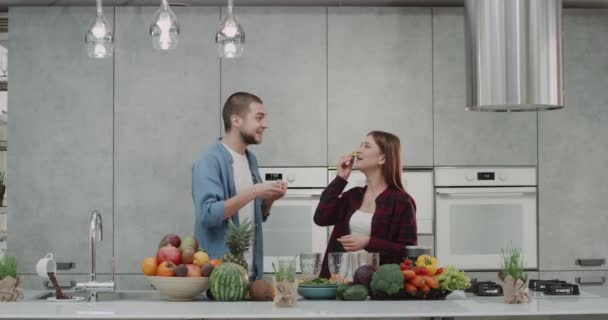 Pareja vegana en la mañana comiendo desayuno saludable, feliz pasar un buen rato en la cocina con increíble isla de la cocina grande y llena de verduras y frutas . — Vídeos de Stock