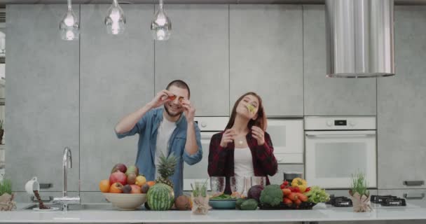 Em uma cozinha moderna, um jovem casal passando um tempo engraçado juntos fazendo bigodes de legumes antes de fazer o café da manhã saudável. . — Vídeo de Stock