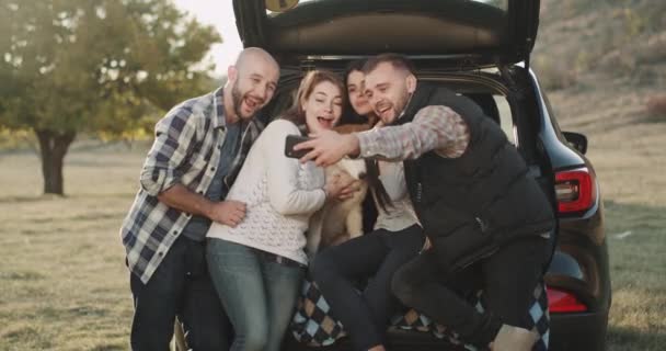 Grupp vänner i en resa som tar selfie med en husky hund i en stam av bilen mitt i naturen. — Stockvideo