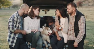 Closeup iki aile ile küçük bir husky köpek ve bir küçük çocuk arabanın bagajına oturan güzel piknik ve birlikte bir görüşme