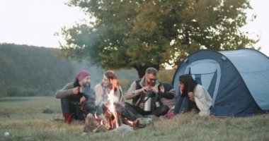 Doğanın ortasında karizmatik iki aile ile çadır, onlar birlikte bir kamp ateşi çay içme termos akşam vakit mutlu yolculuklar.