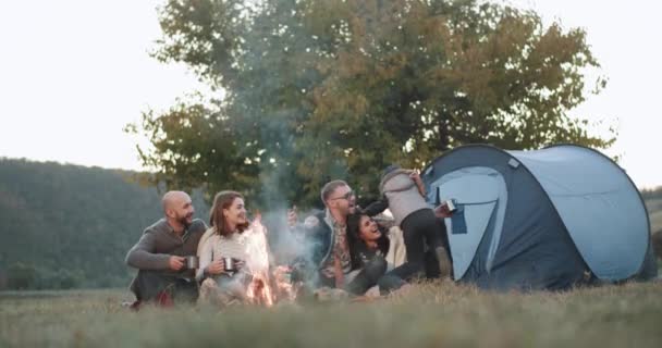Uma bela companhia de jovens, e uma família com um menino pequeno tem uma viagem com uma tenda, à noite eles estão sentados ao redor da fogueira e brincando engraçado. 4k — Vídeo de Stock