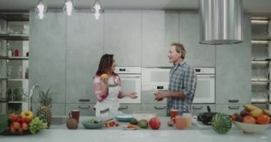 Komik Olgun çift portakal modern bir gri mutfak birlikte kahvaltı yaparken hokkabazlık. 4k