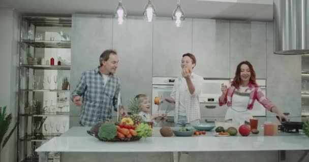 Зрілі батьки зі своїми двома хлопчиками проводять сімейний день разом на кухні, додаючи їжі одночасно 16 років хлопчик жонглює з апельсинами . — стокове відео