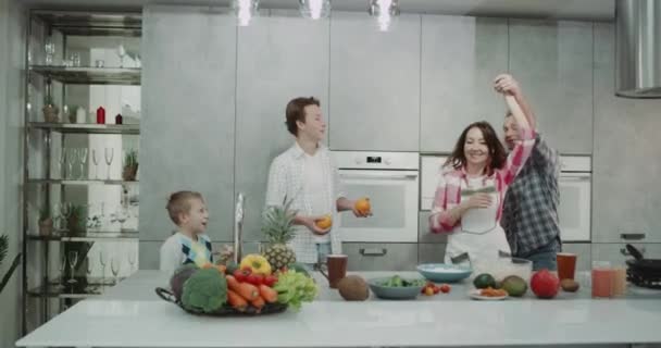 Dacing äldre par i köket med sina två barn, spenderar en bra morgon tillsammans medan du förbereder frukost. — Stockvideo