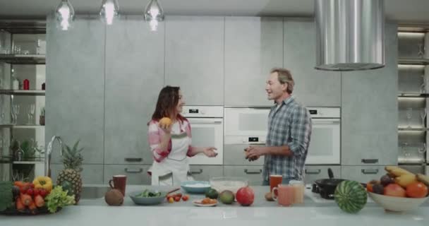 Komik Olgun çift portakal modern bir gri mutfak birlikte kahvaltı yaparken hokkabazlık. 4k — Stok video