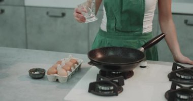 Bir kız onu tavada yağı koyarak ve mükemmellik için onun yumurta baharat.