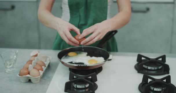 厨师在一个绿色的围裙烹饪四个鸡蛋在一个平底锅, 背景看起来很美观. — 图库视频影像