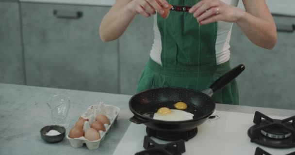 Pişirmek için onun tava içine yumurta çatlama ve sabırla onları bekleyen bir kız. 4k — Stok video