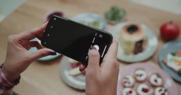 Masaya estetik gıdalar fotoğraf çekmek için telefonunu kullanarak bir kadın. — Stok video