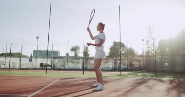 Campo de ténis dia ensolarado, uma senhora bonita equipada para o jogo de ténis movendo-se engraçado antes do jogo . — Vídeo de Stock