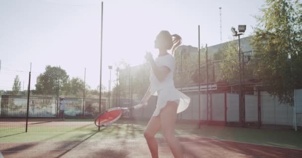 W słoneczny dzień ładna pani w tenis sąd dacing przed rozpoczęciem gry, trzymając w ręku rakieta do tenisa. — Wideo stockowe