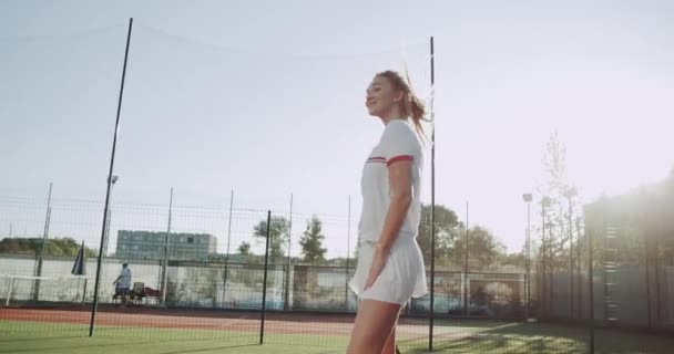 Dacing mulher esportiva no campo de ténis antes de iniciar o jogo, dia ensolarado. 4k — Vídeo de Stock