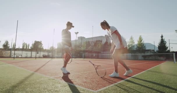 Dos jugadores profesionales damas tienen una pequeña conversación antes de jugar al tenis, golpeando las manos y haciendo para el juego en la cancha de tenis . — Vídeos de Stock