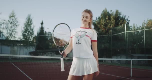 Jugando con una raqueta de tenis una hermosa dama delante de la cámara en la cancha de tenis . — Vídeo de stock