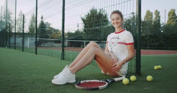 床プロのテニス プレーヤーの女性の上に座って、カメラを見て笑みを浮かべて. — ストック動画