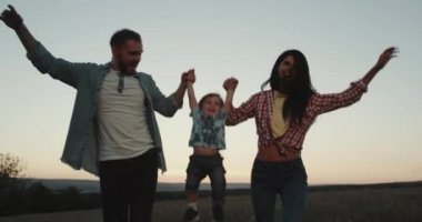 Güzel genç Aile, üç üye, anne baba ve bebek oğulları alan birbirlerine yumruk yumruğa tutan günbatımında yürüyüş mutlu gülümseyerek. 4k
