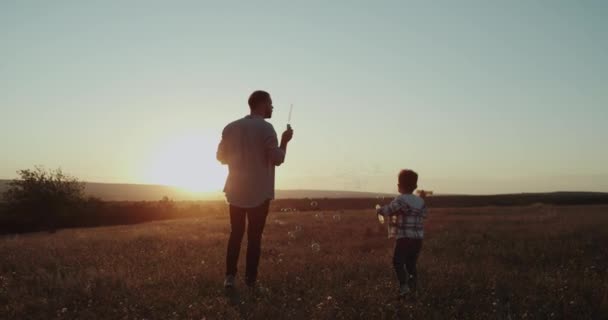 Потрясающие моменты папа и сын делают пузырьки на природе, красивый закат. 4k — стоковое видео
