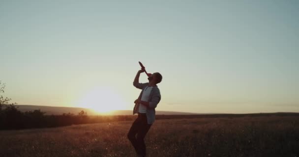 Při západu slunce mladý muž uprostřed pole hrát s velké letadlo. 4k — Stock video