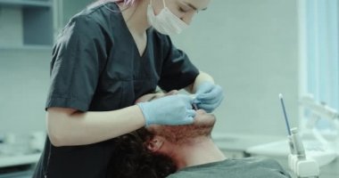 Diş Kliniği Oda genç hasta dentis sandalye ve diş hekimi üzerinde oturan ağızlık ağzını koyar. 4k