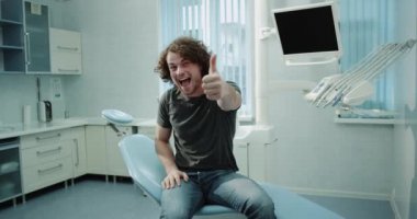 Çok mutlu kamera önünde seyir ve bir büyük gibi gösterilen bir diş denetledikten sonra dentis sandalyede oturan bir diş kliniği odada çok karizmatik genç hasta adam. 4k