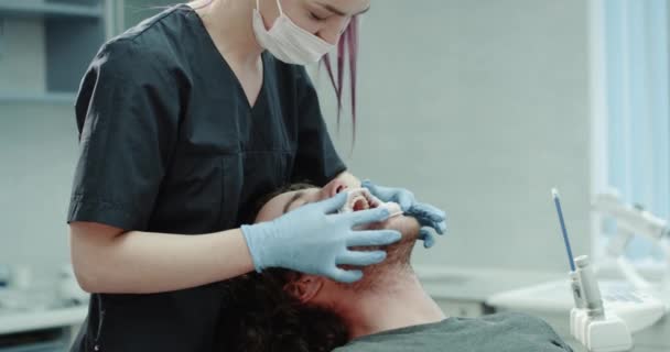 I en modern tandklinik tandläkare fastställande munnen vakt till patienten han rolig titta rakt på kameran och leende. — Stockvideo