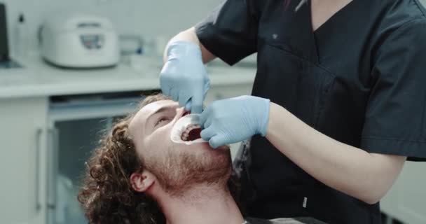 クローズ アップ歯科医院部屋歯椅子に座っていると彼の歯科医口ガードを修正しているまで待っている若い患者. — ストック動画