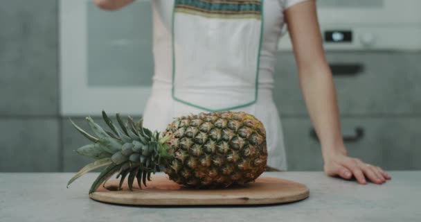 In the kitchen a woman cut a big pineapple with a big knife closeup , slow motion. — Stock Video