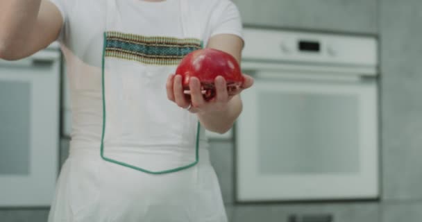 Mulher na cozinha closeup segurando uma romã e mostrar como fácil abrir e limpar a romã com um. movimentos lentos. tiro no épico vermelho — Vídeo de Stock