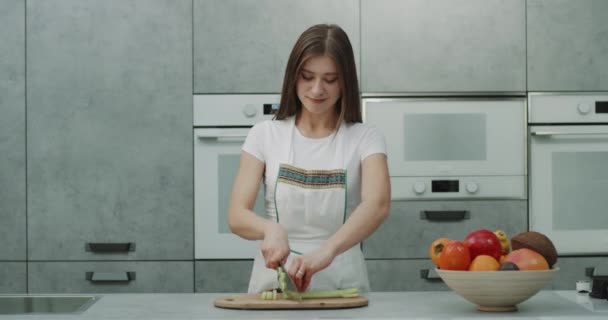 Sorridente abbastanza femminile molto veloce tagliare alcune verdure di fronte alla fotocamera in una cucina moderna e sorridente carino alla fine . — Video Stock