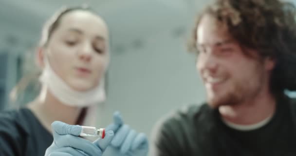 Крупним планом лікар з блакитними рукавичками показує ванну з деякими ліками для свого пацієнта і пояснює, як їх використовувати, вони знаходяться в кімнаті лікарів . — стокове відео