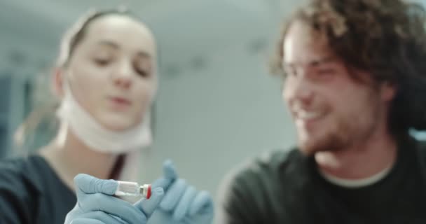 Closeup doctor with blue gloves showing a tub with some medicine to his patient and explain how to be used , they are in the doctors room. — Stock Video