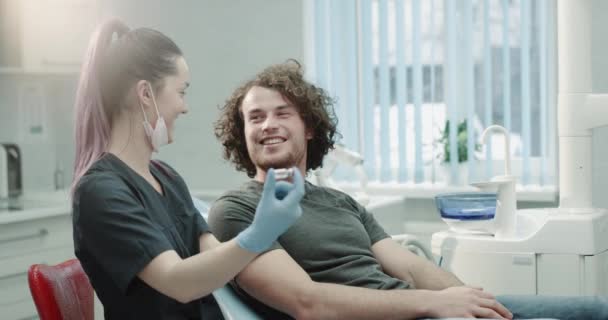 Chez le dentiste jeune patient après une procédure d'hygiène buccodentaire médecin lui donnant un médicament pour utiliser une maison et expliquer les instructions à utiliser il est très confus et souriant en même temps — Video