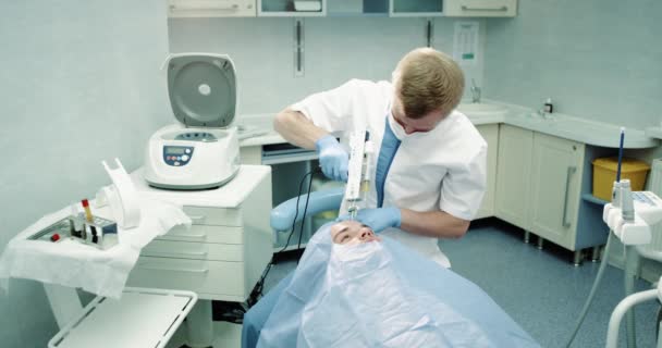 Dans une salle de clinique moderne médecin faire une procédure prp visage vampire avec une micro-aiguille, patient assis sur la chaise de cosmétologie bleue, procédure de mésothérapie . — Video