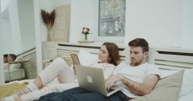Modern yatak odasında yatak ve notebook üzerinde bir şey izlerken onu ortak bir kitap okuma sabah closeup genç bayan.