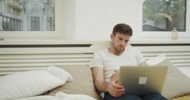 Çok yoğun adam onun laptop modern bir yatak odasında çalışma yatakta döşeme.