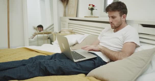 Серйозно людина працює на ноутбуці, сидячи на ліжку . — стокове відео