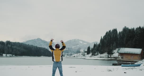 美丽的自然之地在山林和雪湖中间一个快乐的游客欣赏所有的景观在冬季的时间, 快乐的游客穿着黄色夹克和红色的帽子. — 图库视频影像