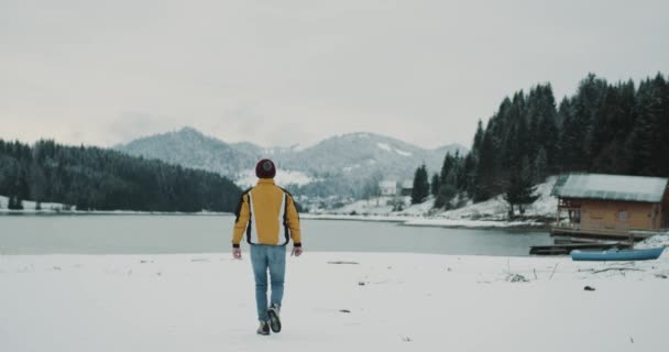 Turista feliz en medio del lago y la montaña admirar toda la belleza de la naturaleza, vista increíble en invierno al lado del lago una pequeña casa de madera, el turista saltando muy eufórico. mociones lentas — Vídeos de Stock