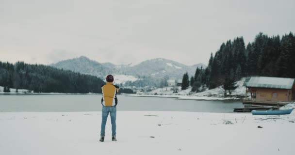 Unga turist man beundra den fantastiska utsikten över sjön och bergen mitt i vintern med snöiga skogen, han är den upprymd av landskapet. 4k — Stockvideo