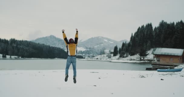 雪に覆われた湖と周り大きな山林 大きな湖のほとりにカメラの前でジャンプ観光男驚くべき場所に先に到着した幸せ大喜びの観光 — ストック動画