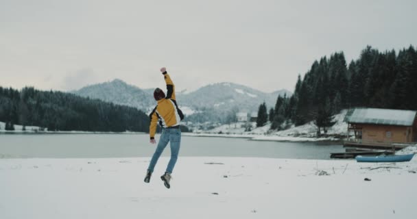 雪に覆われた湖と幸せな若い観光客が彼の目的地に到着した大きな森と山の美しい風景は、すべての周りジャンプ彼大喜びの自然の美しさをお楽しみください。4 k — ストック動画