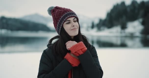 Retrato de una joven que mira directamente a la cámara sonriendo a lo grande tiene un aparato ortopédico blanco, señora con un sombrero rojo de pie frente a la cámara en un lugar natural increíble con un bosque cubierto de nieve y un — Vídeo de stock